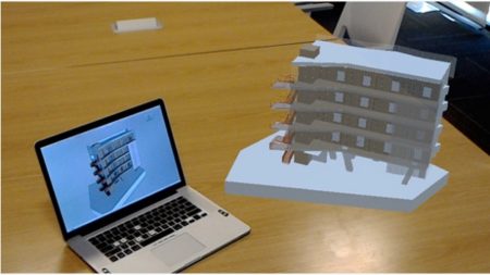 03 - In this image we see a user wearing a Microsoft Hololens while looking at their SketchUp model at a particular scale within the context of their physical surroundings which happen to show a MacBook running SketchUp with the model loaded. 